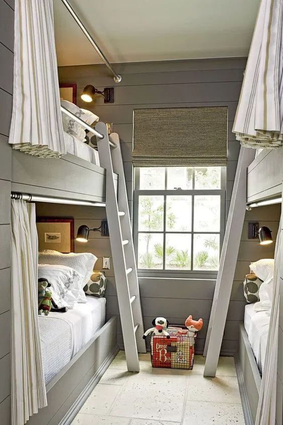 a modern grey kids' room with built-in bunk beds, neutral and grey bedding, ladders and striped curtains plus black sconces