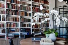 a modern home library with built-in bookshelves in white and a large round table and black leather chairs