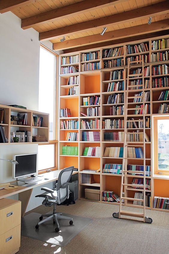 a modern home office with a large shelving unit plus orange backing and a cool desk