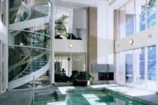 a modern house with large windows and a glass-encased taircase, with a fireplace and a lit up pool is a great space to live in