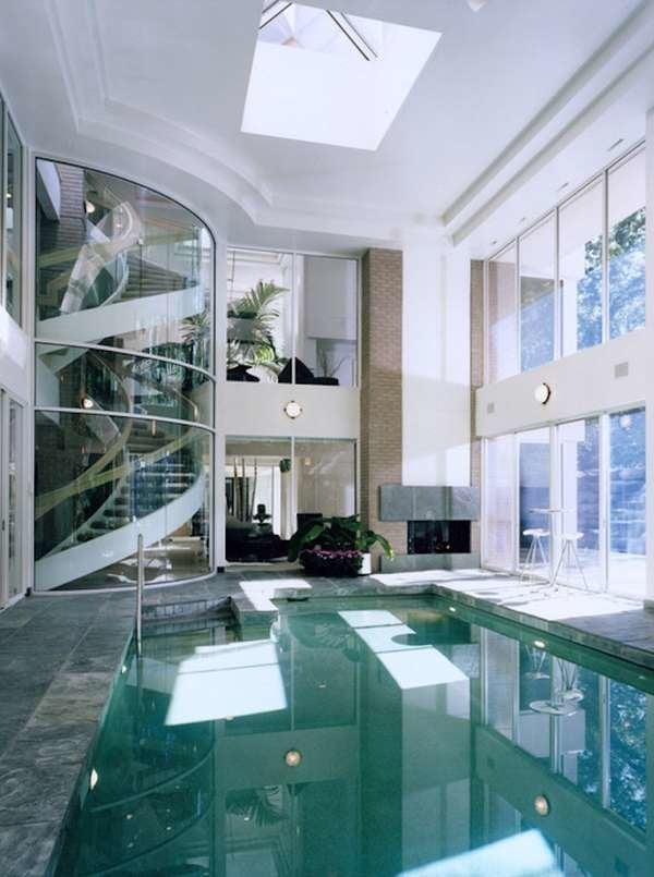a modern house with large windows and a glass-encased taircase, with a fireplace and a lit up pool is a great space to live in