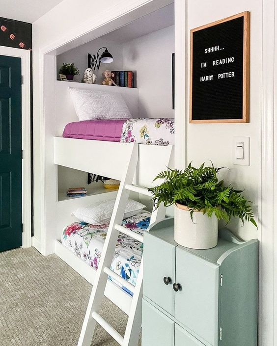 a modern kids' room with built in beds, printed bedding, a ladder, a green storage unit, a chalkboard and some lamps and lights