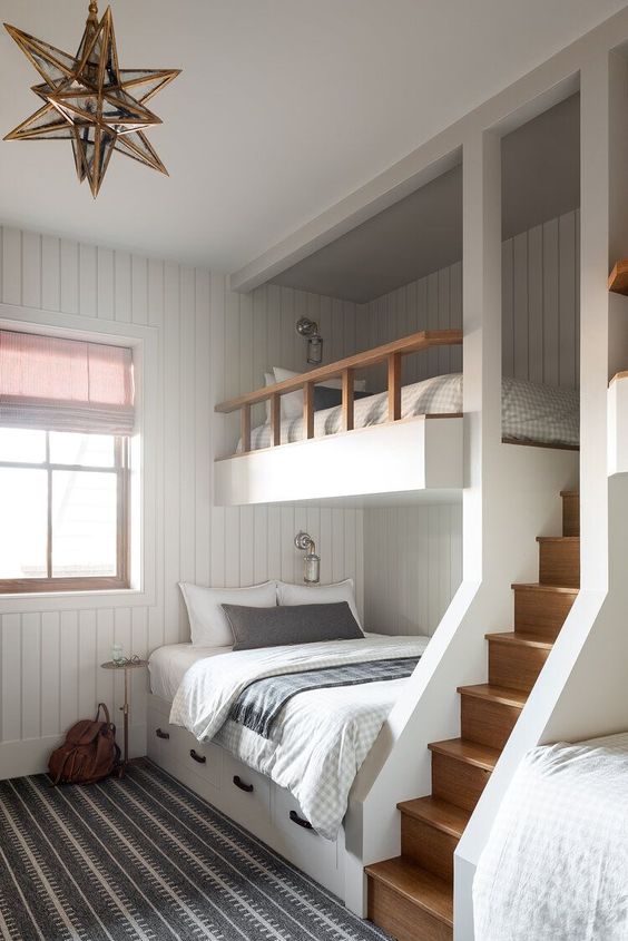 a modern kids' room with white shiplap walls, built-in bunk beds with printed bedding, a gold star-shaped pendant lamp and a ladder