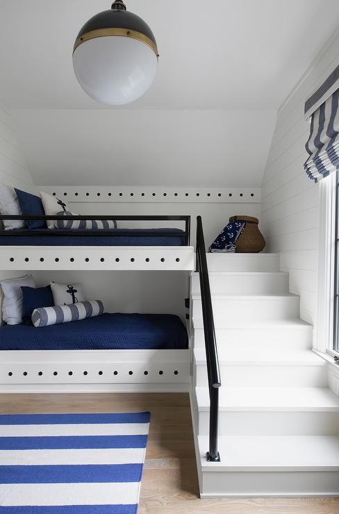 a modern nautical kids' room with built-in bunk beds, navy and white bedding, a striped rug and some pretty decor