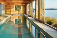 a modern wooden pool house with glazed walls that are sliding and a large pool plus a gorgeous sea view