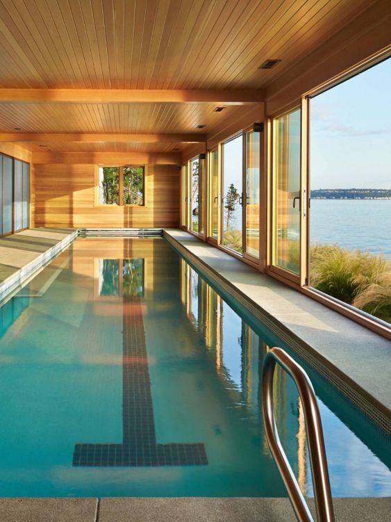 a modern wooden pool house with glazed walls that are sliding and a large pool plus a gorgeous sea view