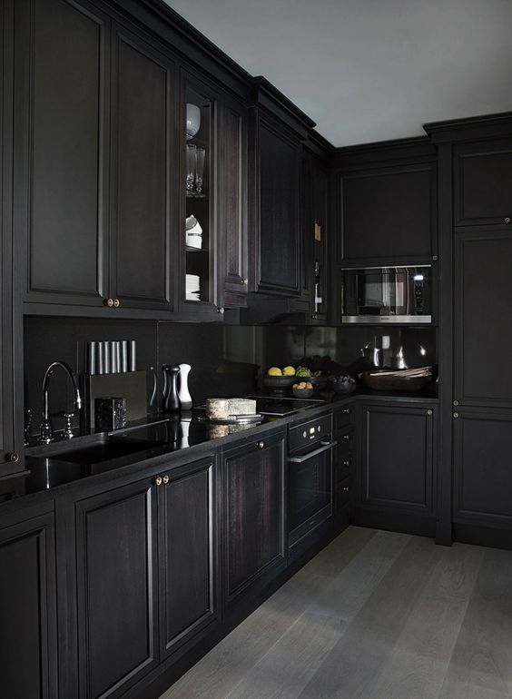a moody black kitchen with shaker cabinets, a black backsplash and countertops, black fixtures is a cool and chic space