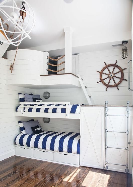 a nautical kids' bedroom clad with white shiplap, with built in bunk beds, a metal ladder and a ship part on top