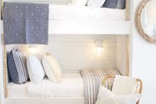 a nautical kids’ room with white shiplap walls, built-in bunk beds, grey and white bedding, a rattan chair, baskets for storage