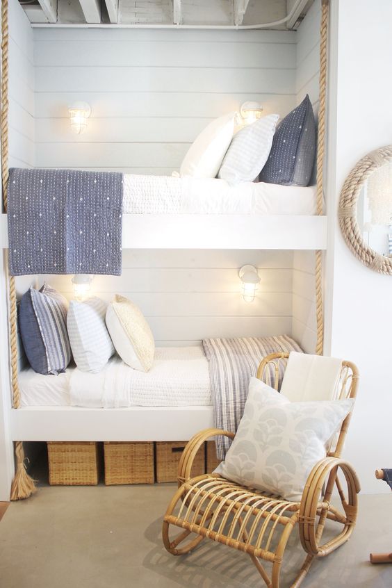 a nautical kids' room with white shiplap walls, built-in bunk beds, grey and white bedding, a rattan chair, baskets for storage