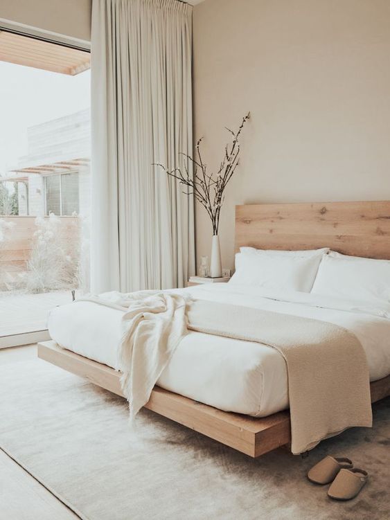 a neutral and airy bedroom is small but looks larger thanks to a neutral color scheme and a glass wall that brings much light