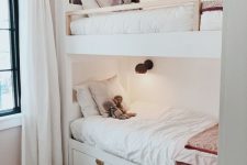 a neutral and welcoming kids’ room with white built-in bunk beds, neutral bedding, sconces and neutral textiles is a very cozy space to be in