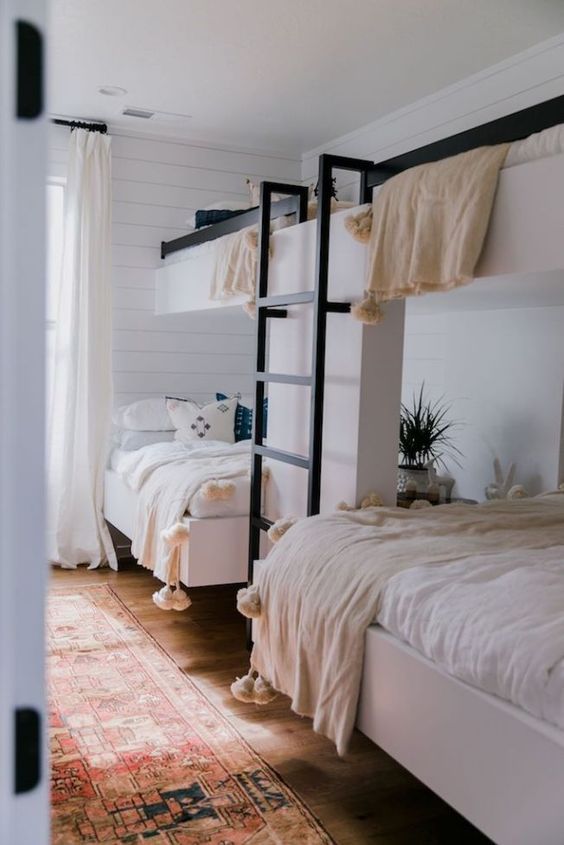 a neutral boho kids' room with bink beds, a ladder, neutral bedding, a boho printed rug and potted plants