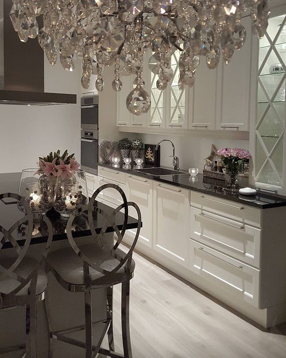 a neutral glam kitchen with black countertops, shiny silver stools, a crystal chandelier and pink florals