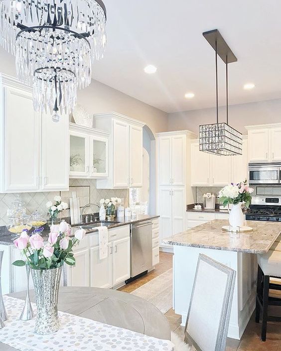 a neutral glam kitchen with white cabinetry, grey stone countertops, shiny crystal chandeliers and grey tiles