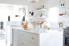 a neutral glam kitchen with white cabinets, white marble countertops and a backsplash, gold handles, a crystal chandelier