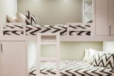 a neutral kids’ room with built-in bunk beds, printed bedding, built-in shelves, a ladder and drawers for storage