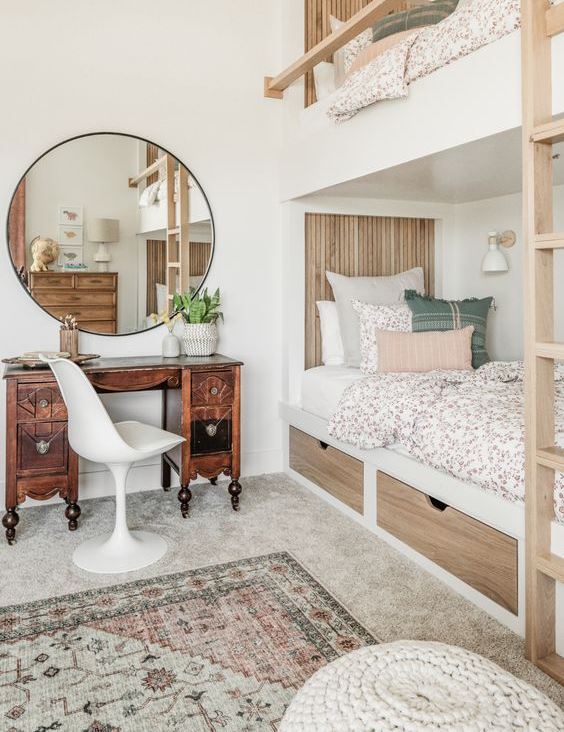 a neutral modern kids' room with built-in bunk beds, printed bedding, a vintage stained desk and a round mirror, printed rugs