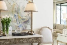 a neutral refined space with an inlay console table, an upholstered bench, a neutral antique chair and some table lamps