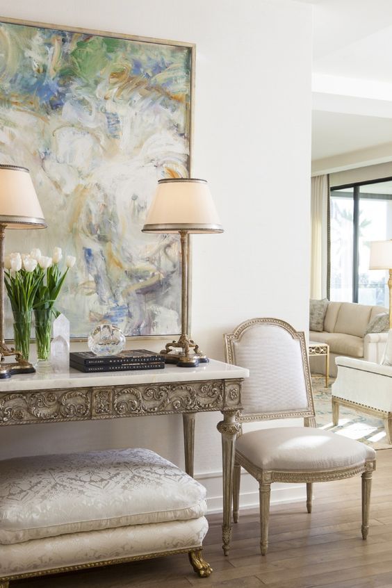 a neutral refined space with an inlay console table, an upholstered bench, a neutral antique chair and some table lamps