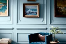 a pastel blue room with molding on the walls, a blue upholstered chair, a gallery wall, some coffee tables and a bench is amazing