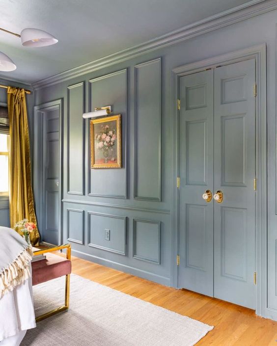 a pastel blue room with molding on the walls and doors, with gold and mustard touches and a pretty mauve chair