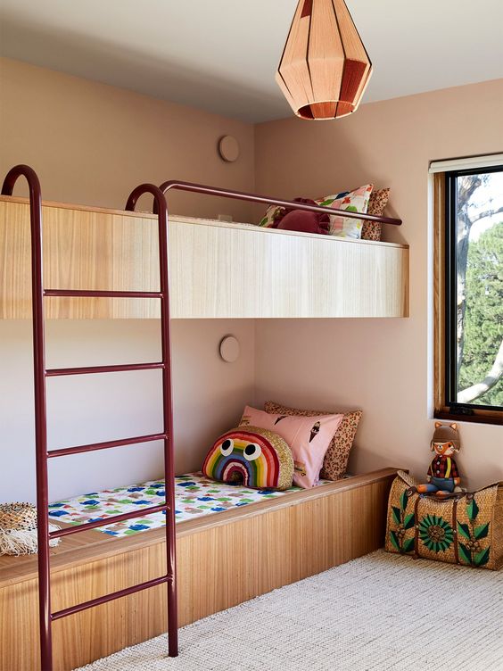 a pastel boho shared girls' bedroom with built-in bunk beds, a metal ladder, printed bedding and pillows and a cool pendant lamp