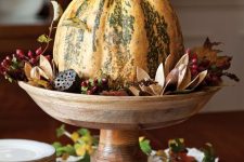 a pumpkin with dried blooms, berries, leaves and lotus on a wooden stand is a lovely rustic centerpiece to make