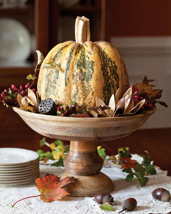 a pumpkin with dried blooms, berries, leaves and lotus on a wooden stand is a lovely rustic centerpiece to make