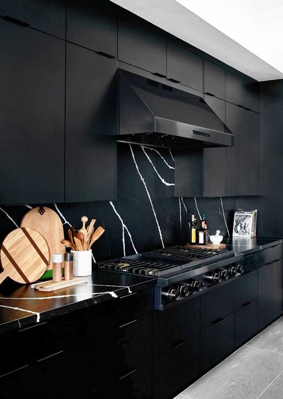 a refined black kitchen with metal cabinets, a marble backsplash and countertops and a black hood