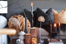 a refined coffee table arrangement with a modern candelabra with black candles, a trya with perforated candle holders and dried branches and herbs