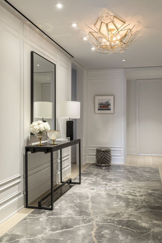 a refined contemporary entryway with molding on the walls, a dark glass console, a large mirror, a catchy geometric chandelier