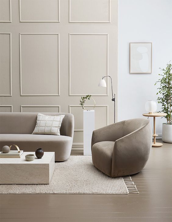a refined contemporary space in white and grey, with molding, curved furniture, a stone slab coffee table and greenery