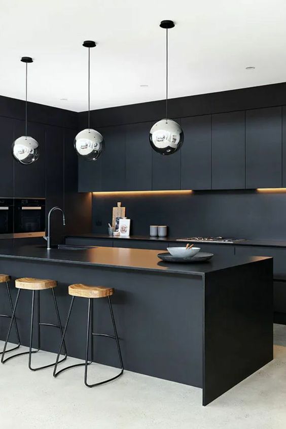 a refined minimalist black kitchen with sleek cabinets, a matte backsplash and countertops, tall stained stools and polished metal pendant lamps