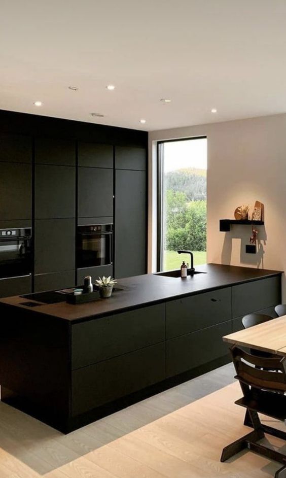 a refined minimalist black kitchen with sleek cabinets, brown countertops, built-in appliances and a small dining space