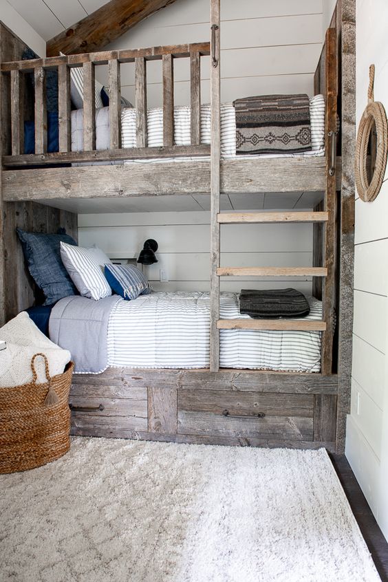 a rustic kids' room with aged reclaimed kids' bunk beds, printed and neutral bedding, a basket with bedding and black sconces on the walls