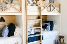 a rustic kids’ room with four built-in bunk beds, white, blue and navy bedding, a ladder and lots of pillows and black sconces