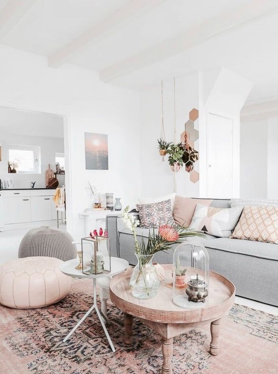 a serene living room with a low grey sofa, a boho printed rug, a grey and a pink pouf, some pink pillows and a carved wooden table