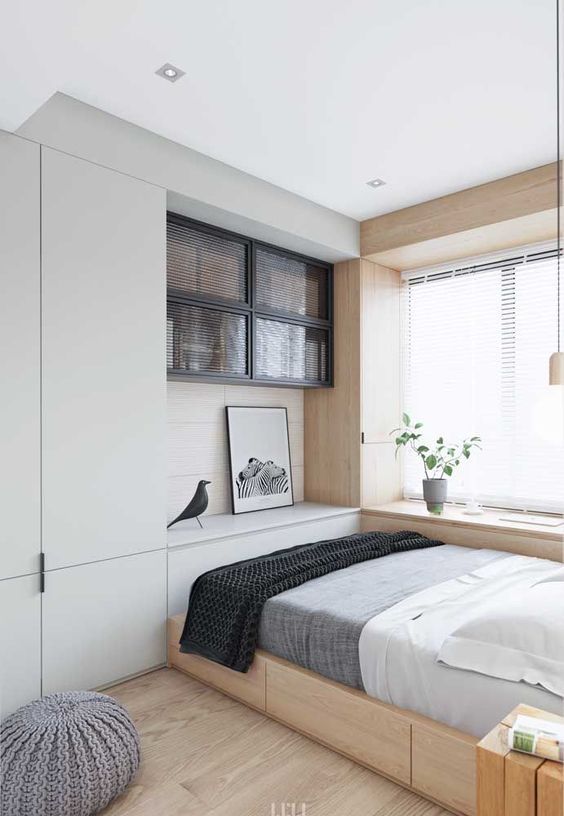 a small bedroom looks larger thanks to the neutral color scheme, a large window by the bed and floor to ceiling furniture