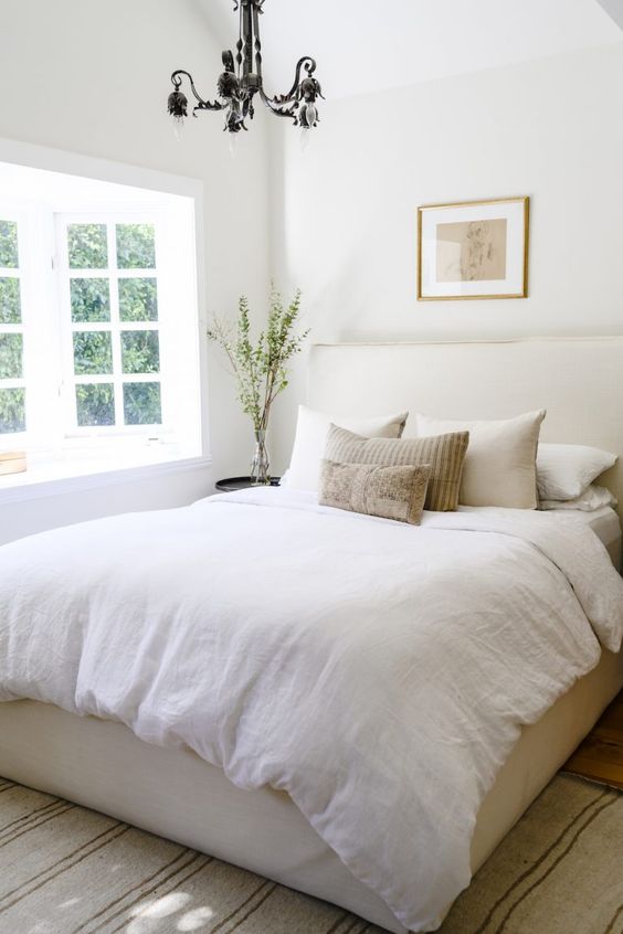 a small bedroom with a neutral color scheme and a bay window that brings much light inside looks bigger