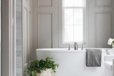 a soothing bathroom with grey walls with molding, an oval tub, a potted plant and a vintage-inspired chandelier