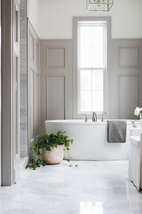 a soothing bathroom with grey walls with molding, an oval tub, a potted plant and a vintage-inspired chandelier