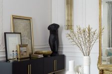 a sophisticated Parisian living room with molding on the walls, gold touches, a black credenza, a gold coffee table and an oversized mirror