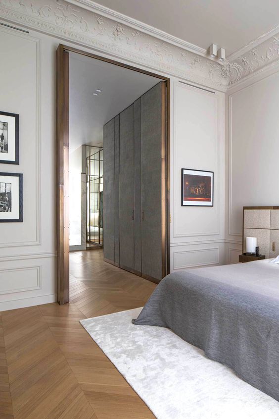 a sophisticated bedroom with molding on the walls and ceiling, artworks, a bed with cool bedding, neutral upholstered headboard