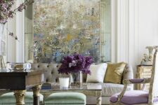 a sophisticated pastel space with an impressionalist artwork, a neutral sofa, an antique lilac chair, green stools and a dark-stained table