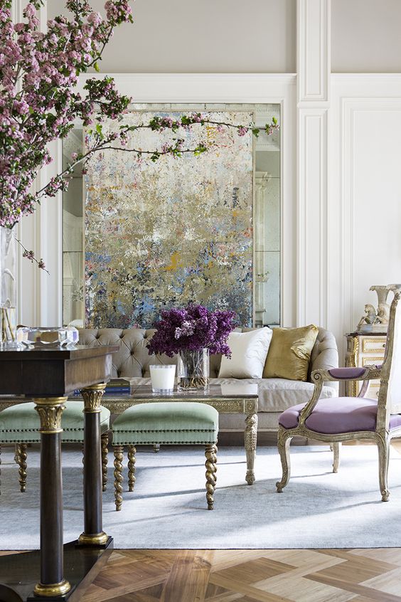 a sophisticated pastel space with an impressionalist artwork, a neutral sofa, an antique lilac chair, green stools and a dark-stained table