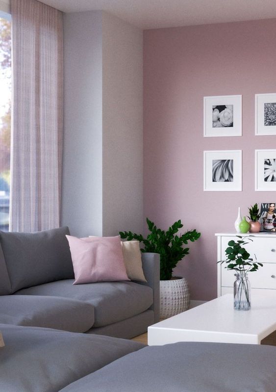 a stylish Scandinavian living room with a pink accent wall, a large grey sectional, white furniture and a gallery wall