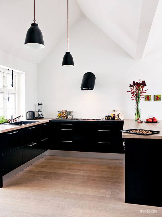 a stylish black contemporary kitchen with only lower cabinets, beige stone countertops, black pendant lamps and a black hood