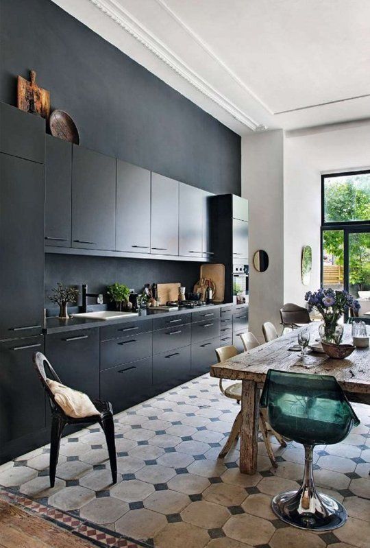 a stylish black kitchen with a matte black wall, black countertops and a backsplash, a rough wooden table and mismatching chairs