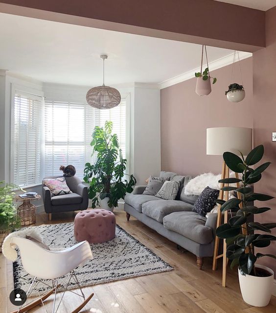 a stylish living room with dusty pink walls, a grey sofa, a grey chair, a white one, potted greenery